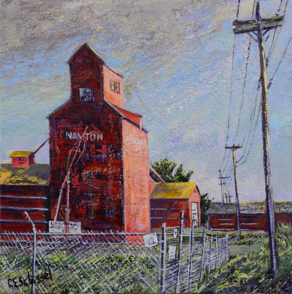 Red grain elevator labeled "Nanton" with buildings, wire fence, cloudy sky, power lines nearby.